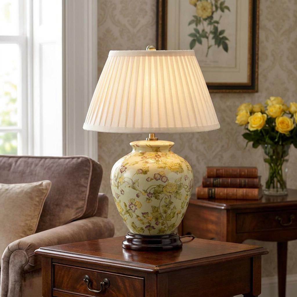 Yellow floral ceramic table lamp with a pleated shade illuminated on a wooden side table.