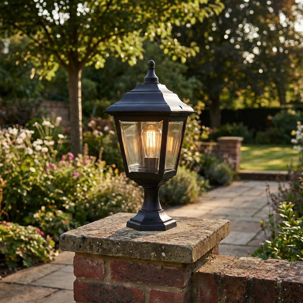 Black lantern outdoor light with an Edison bulb mounted on a brick pillar in a lush garden.