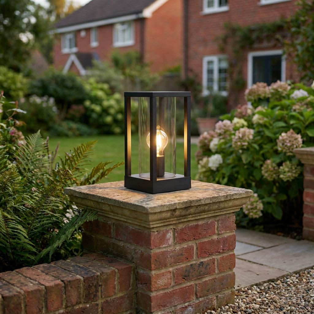 Modern black rectangular lantern with a warm bulb mounted on a brick garden pillar.