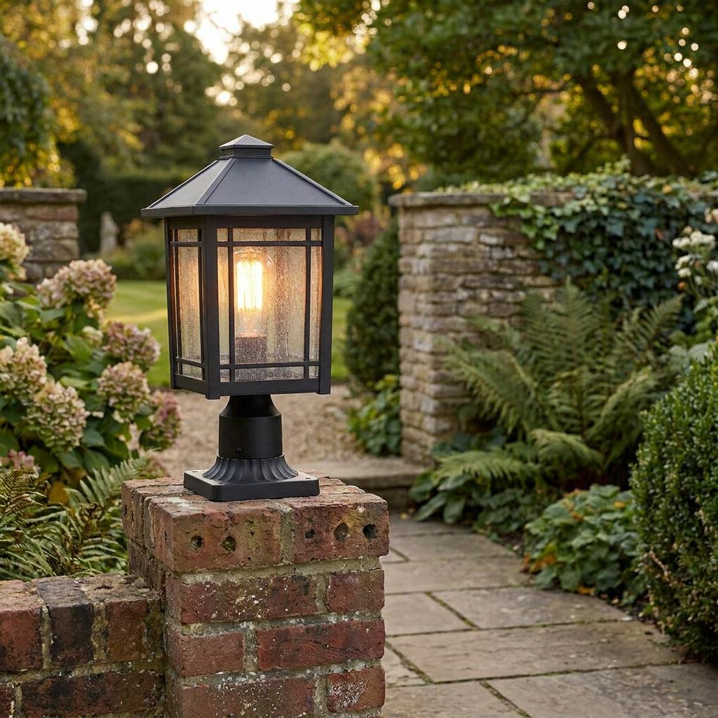 Black traditional pedestal lantern with seeded glass and a warm Edison bulb on a garden brick wall.