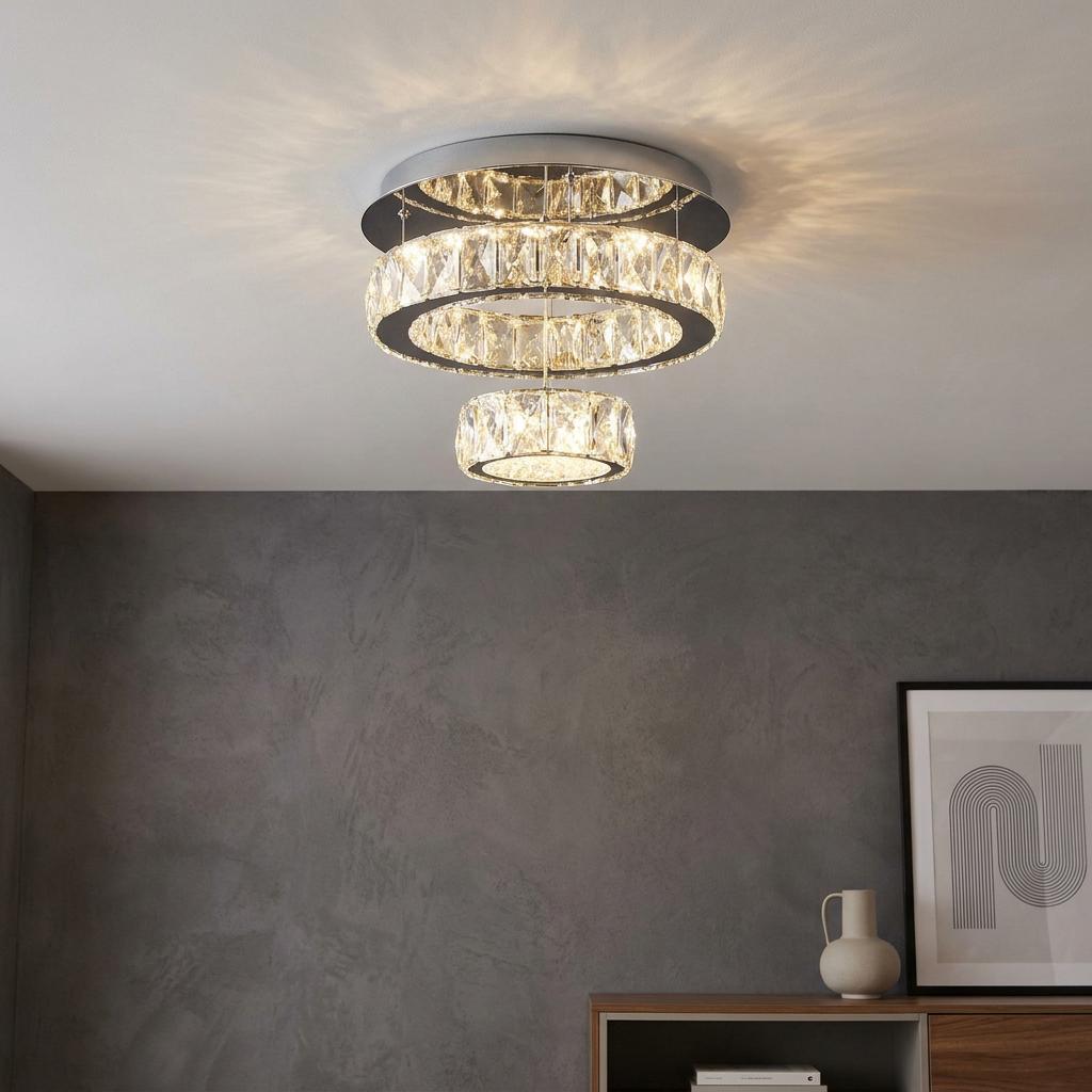 Two-tier crystal LED flush mount ceiling light with chrome finish glowing in a room with grey walls.
