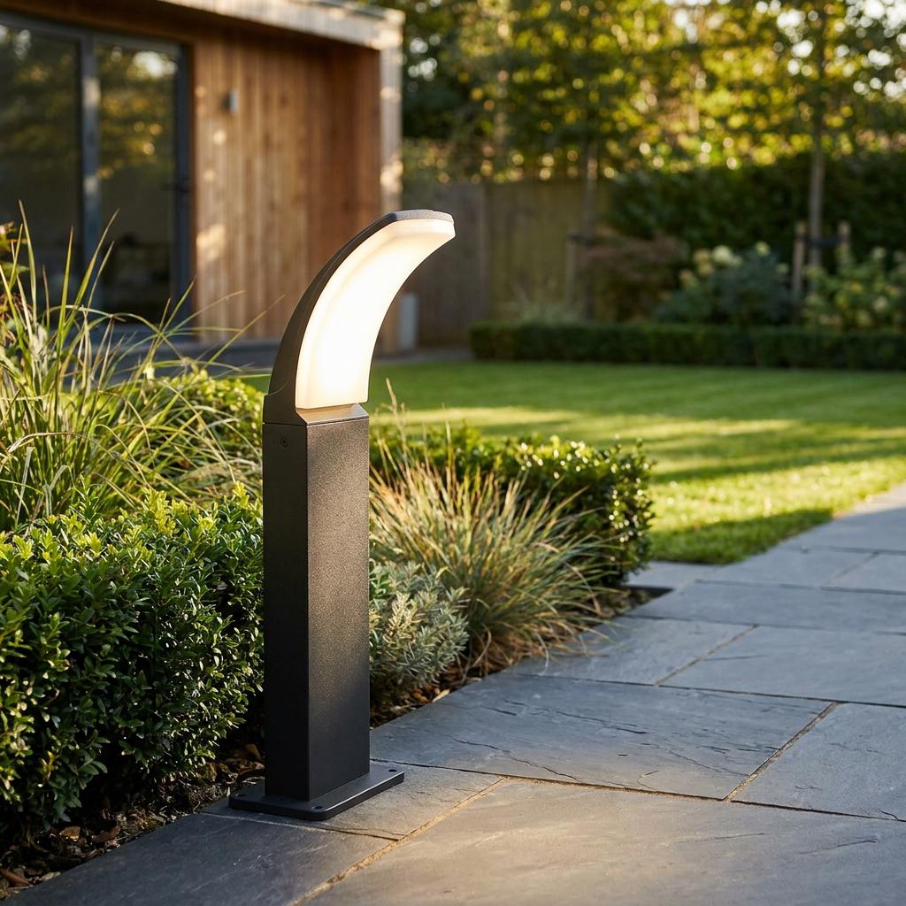 Curved black LED bollard light illuminating a grey slate garden path alongside lush green shrubs and lawn.