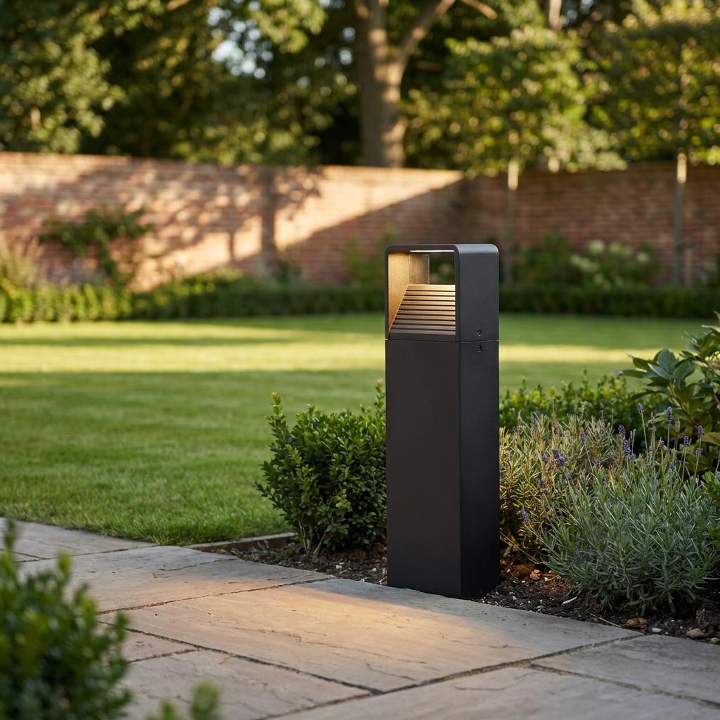 Modern black bollard light casting warm light onto a stone garden path and lawn.