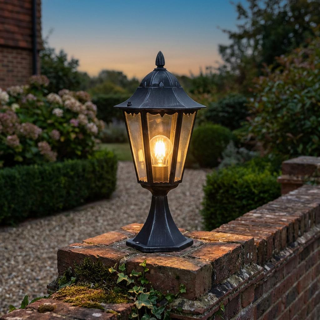 Traditional black outdoor lantern with a warm glowing bulb mounted on a brick garden wall at twilight.