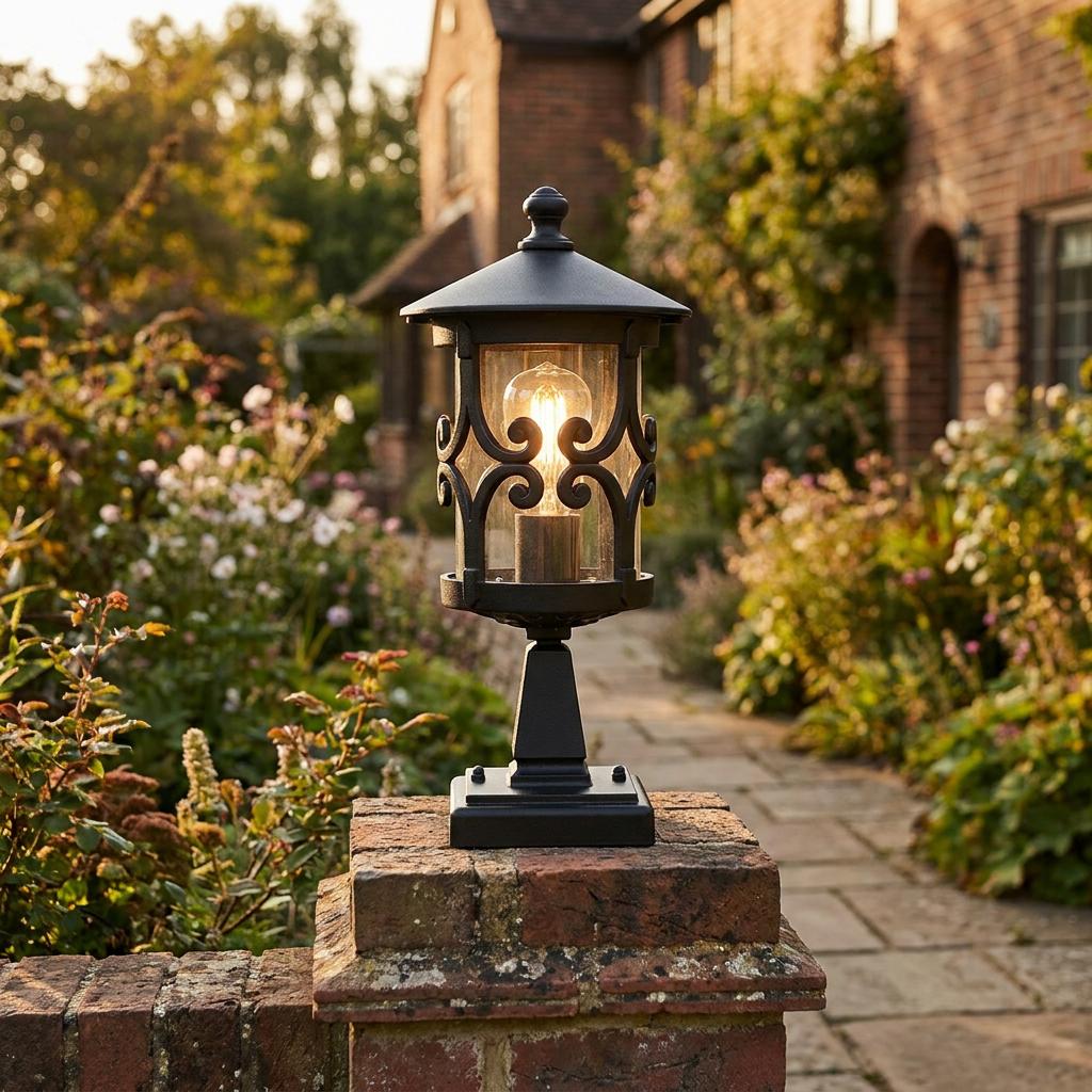 A traditional black outdoor pedestal lantern with decorative scrollwork illuminated on a garden brick pillar.