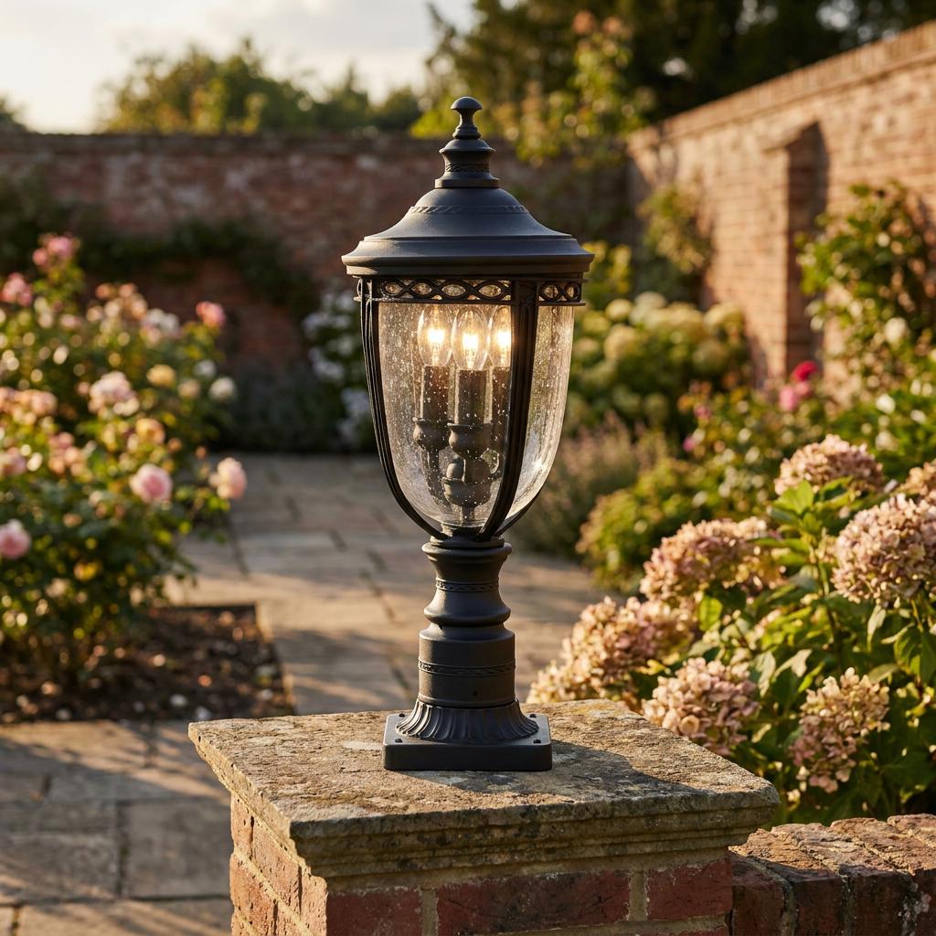 Traditional black outdoor pedestal lantern with three bulbs lit on a brick pillar in a sunny garden.