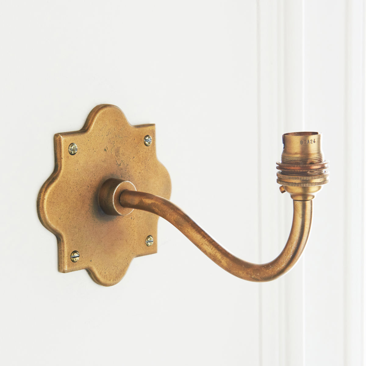 Anvil Curve antique brass wall light mounted on a white panelled wall, arm sweeping out to a brass lampholder