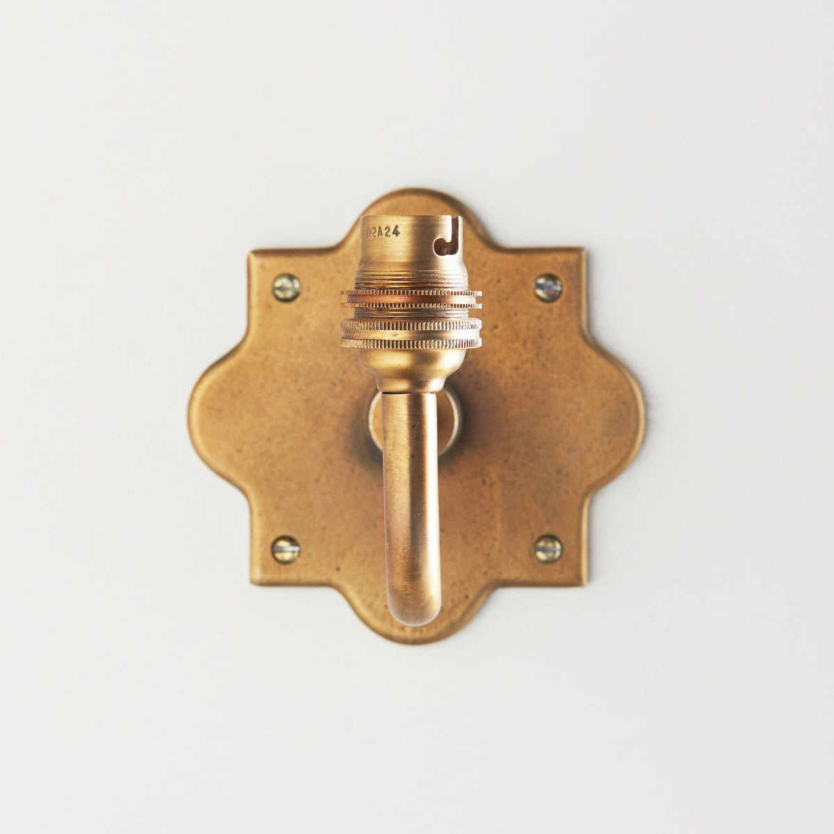 Head-on view of the Anvil Curve wall light showing the scalloped brass backplate and forward-facing lampholder