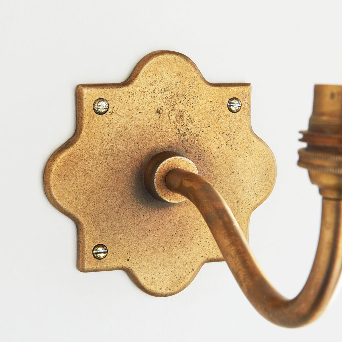 Detail of the scalloped antique brass backplate of the Anvil Curve wall light with visible fixing screws