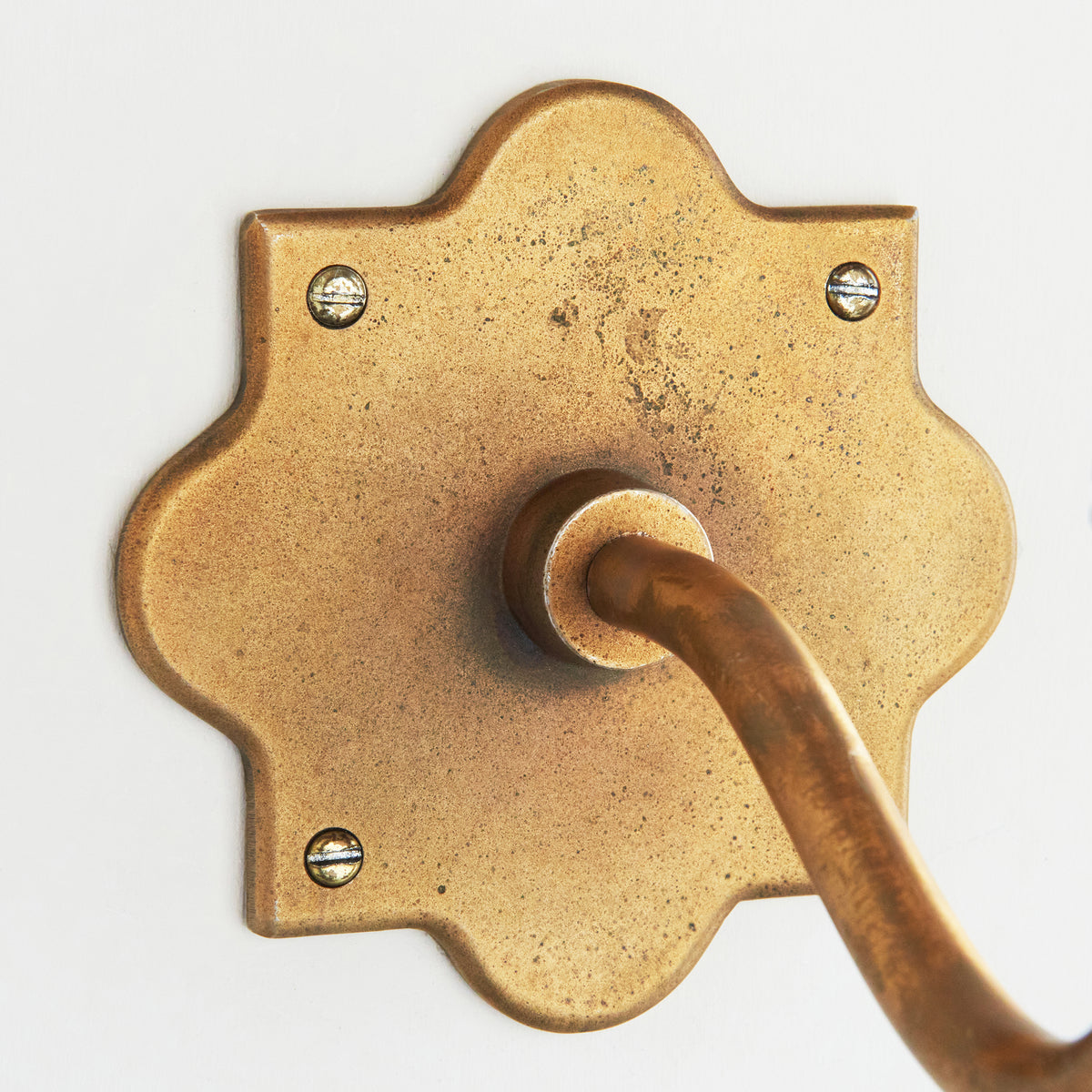 Close crop of the aged brass backplate and arm joint on the Anvil Curve wall light