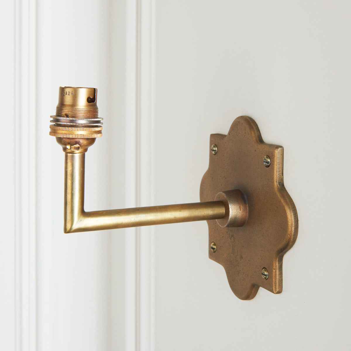 Anvil Angle antique brass wall light fitted to white panelling, its angled arm rising to a brass lampholder