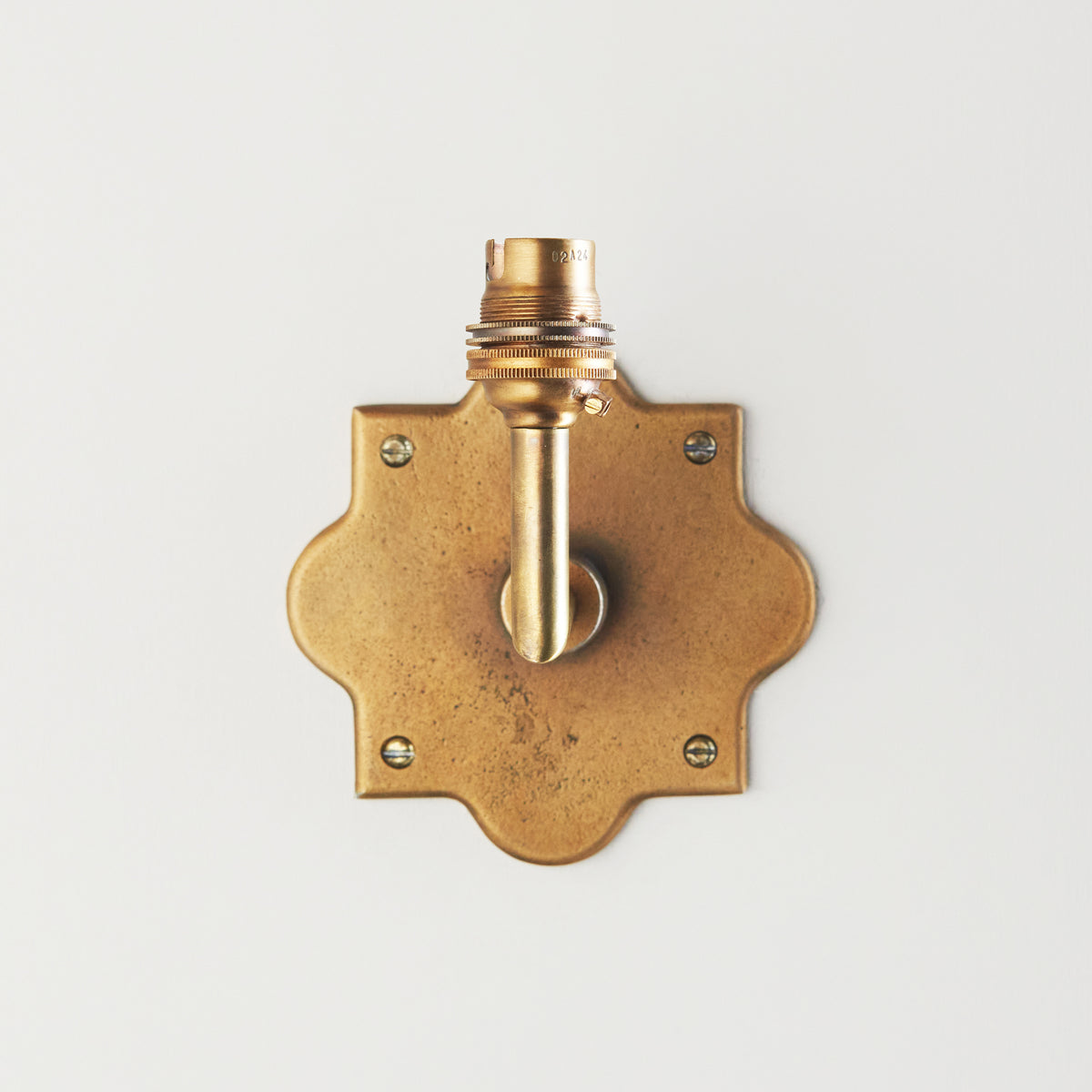 Head-on view of the Anvil Angle wall light showing its scalloped brass plate and upright lampholder