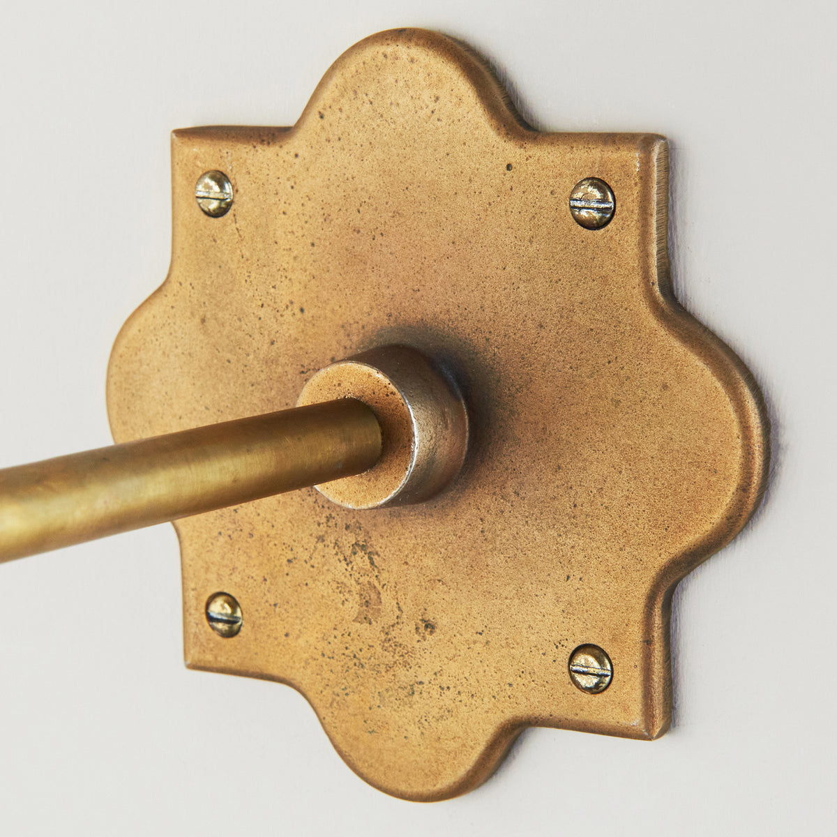 Close-up of the textured aged brass backplate where the Anvil Angle wall light's arm meets the wall