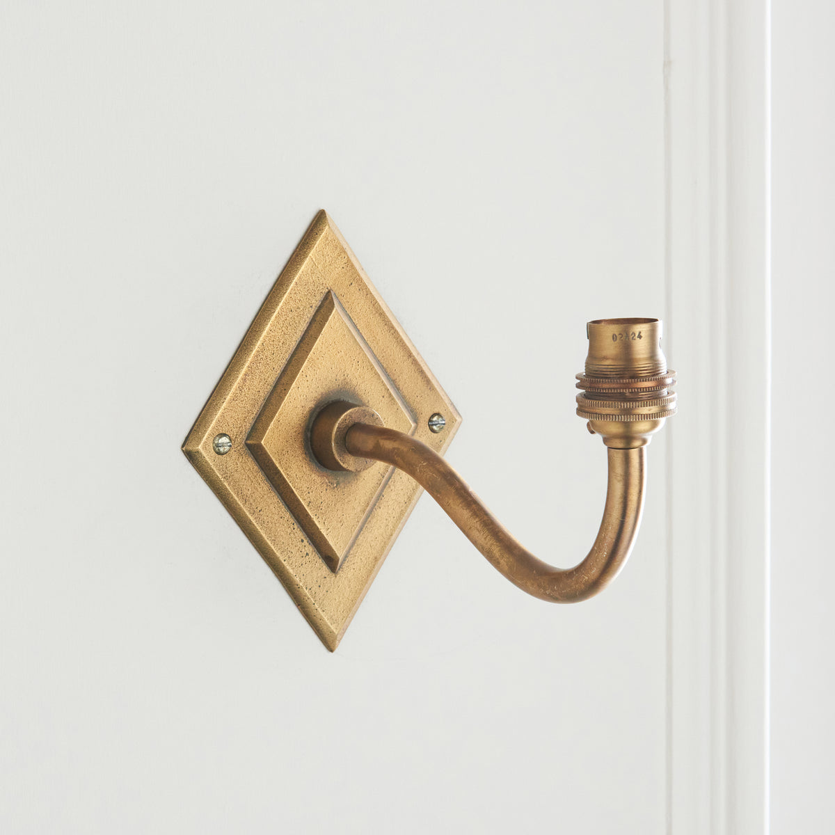 Diamond Curve antique brass wall light on white panelling, curved arm reaching out to a bare lampholder