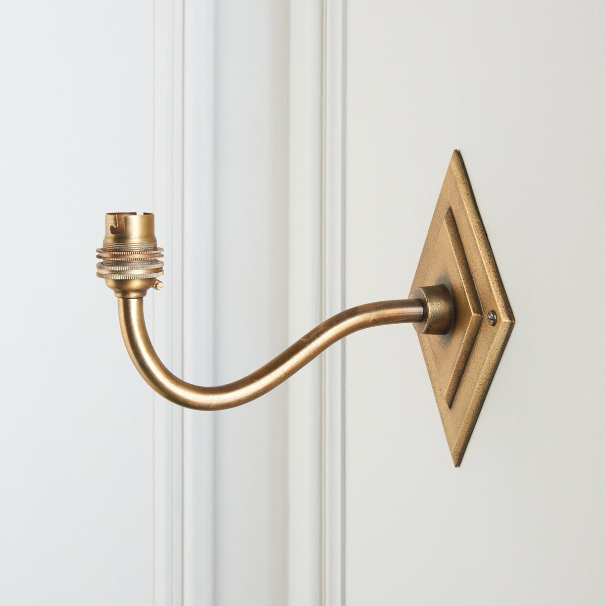 Side view of the Diamond Curve wall light, its brass swan-neck arm extending from a diamond backplate