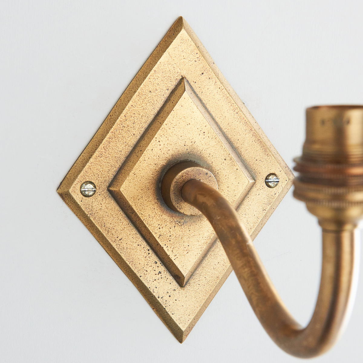 Detail of the antique brass diamond backplate and curved arm of the Diamond Curve wall light