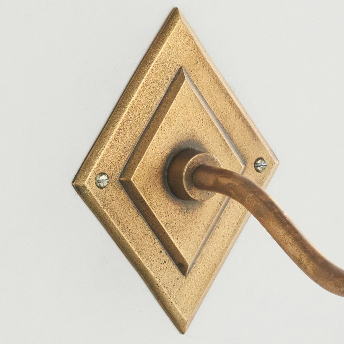 Close crop of the diamond-shaped aged brass backplate on the Diamond Curve wall light