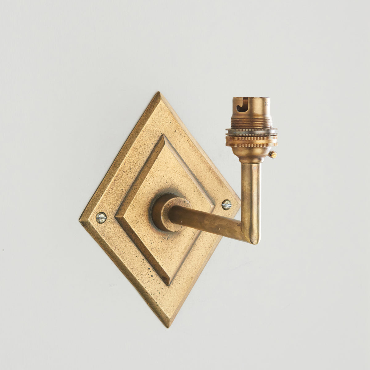 Diamond Angle antique brass wall light against a pale wall, its angled arm topped with a bare lampholder