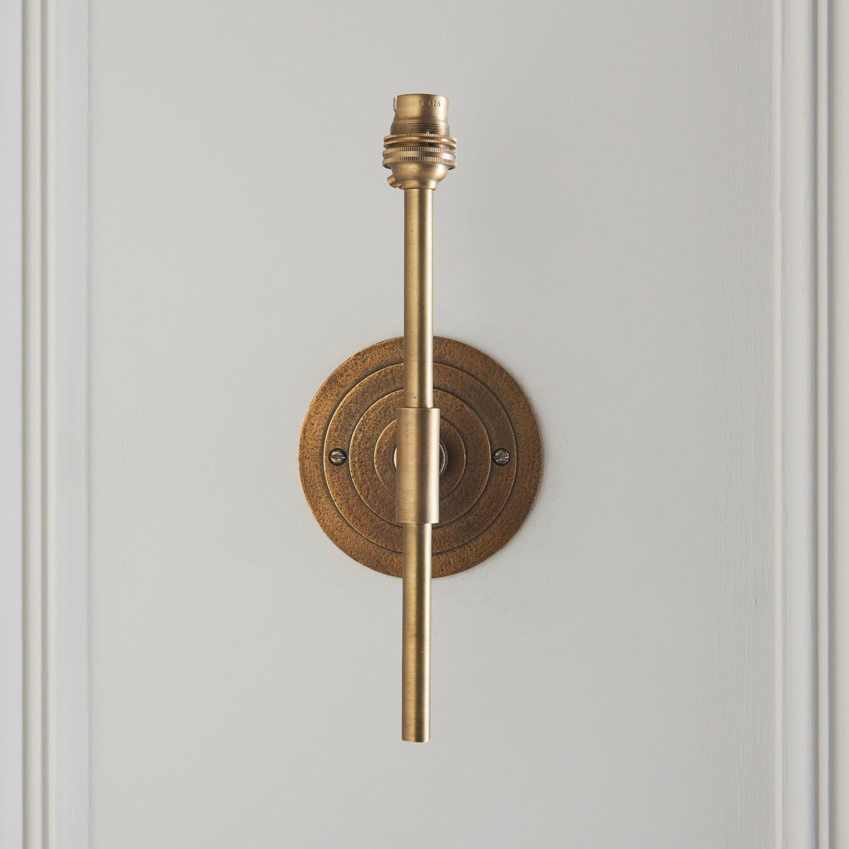 Head-on view of the Halo Tall wall light with concentric ringed brass backplate and upright stem