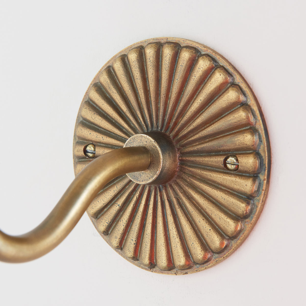 Detail of the Dahlia Swan wall light's fluted brass rose and the arm emerging from its centre