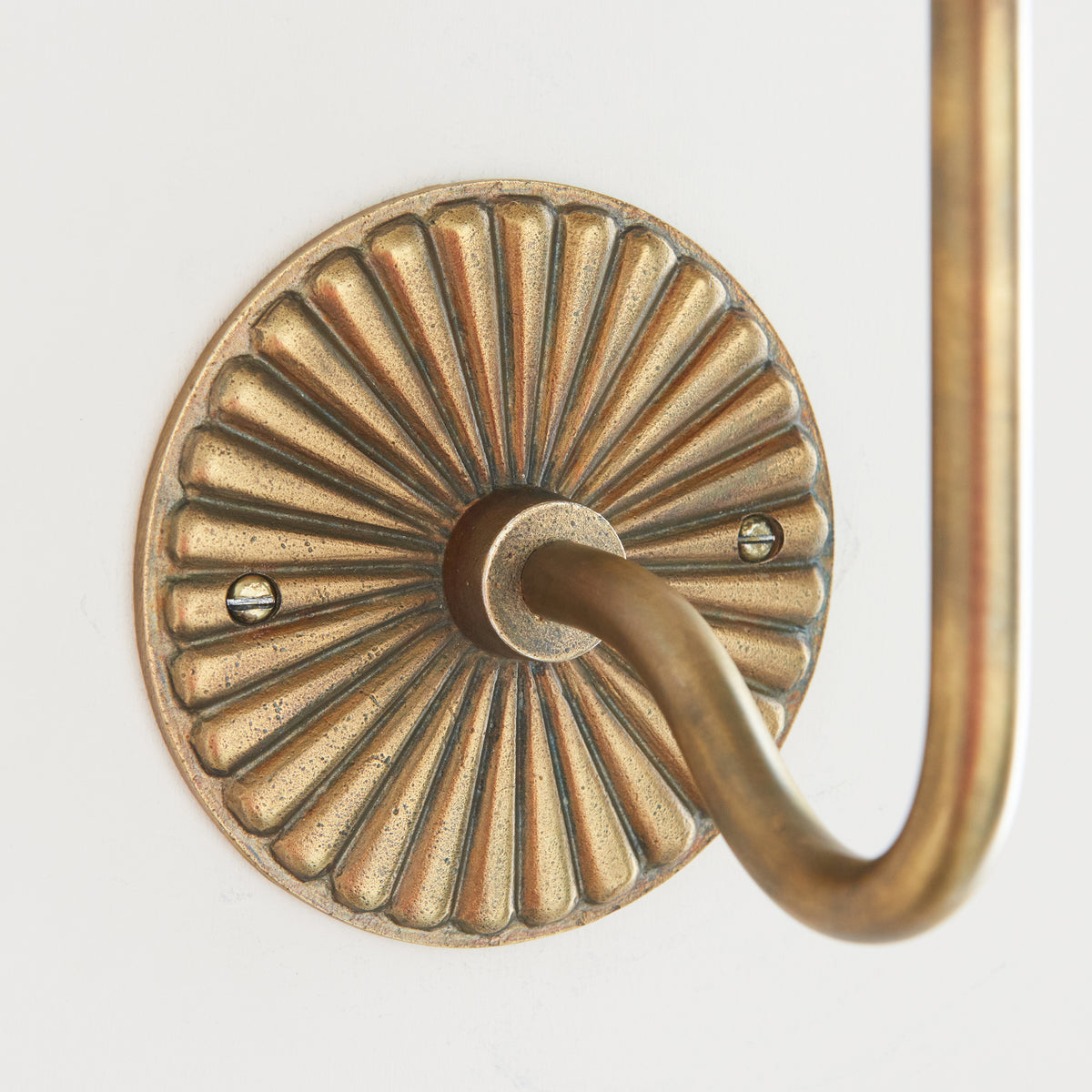 Close crop of the fluted brass backplate and curved arm on the Dahlia Swan wall light