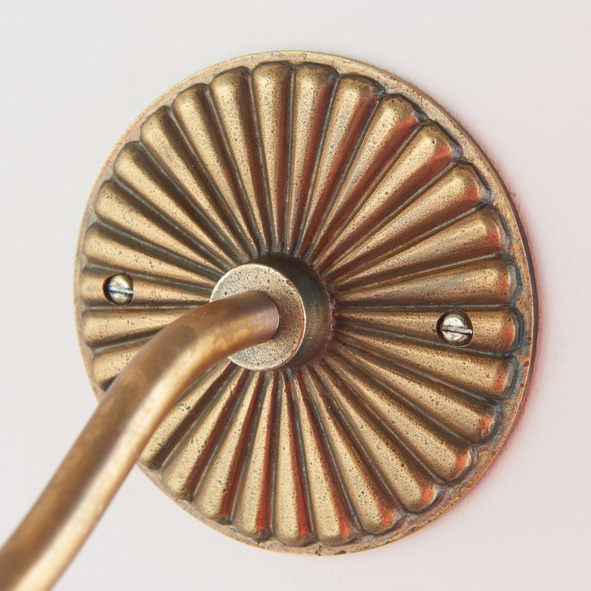 Detail of the fluted antique brass backplate of the Dahlia Curve wall light with the arm sweeping out