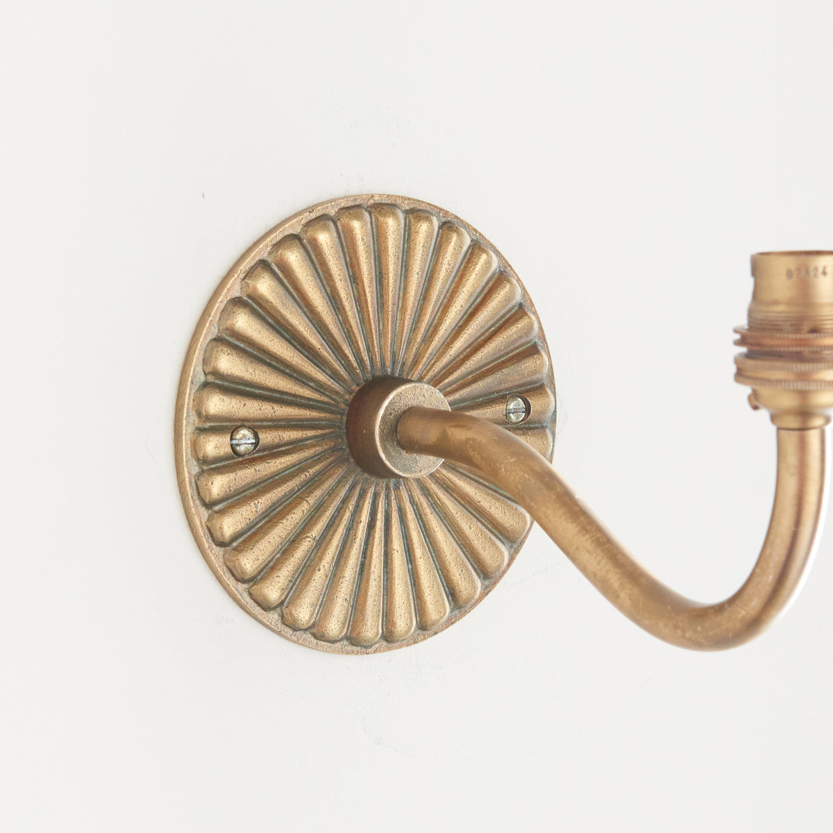 Close-up of the Dahlia Curve wall light's petal-ribbed brass rose and curving arm