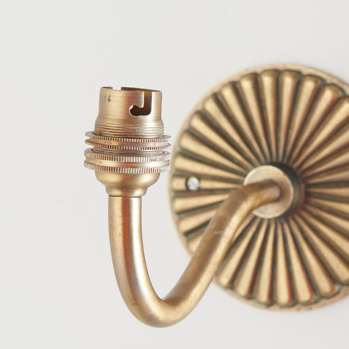 Detail of the ribbed brass lampholder and curved arm of the Dahlia Curve wall light beside its fluted plate
