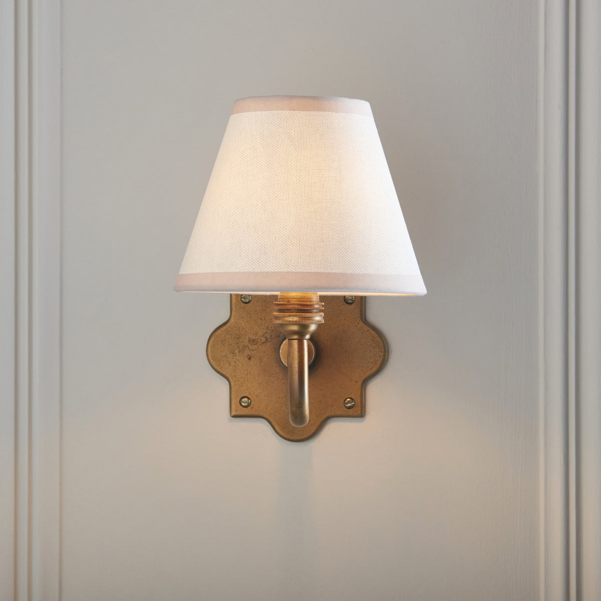 Head-on view of the Anvil Curve wall light showing its ivory empire shade and scalloped brass plate