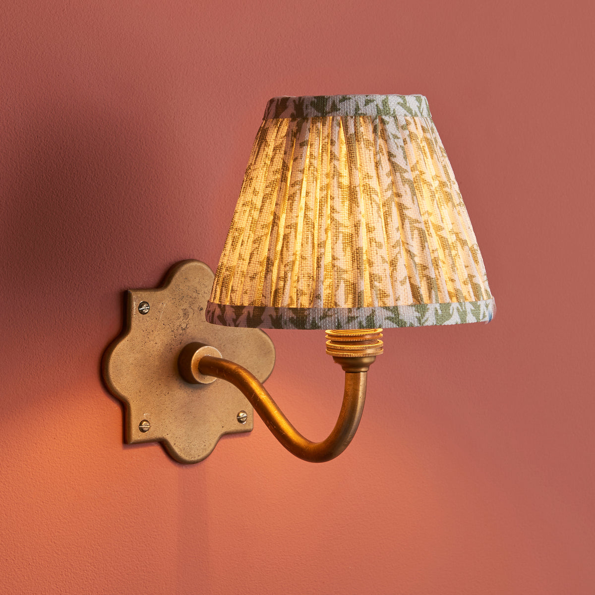 Anvil Curve wall light on a terracotta wall, warm glow through the green leaf-print pleated shade