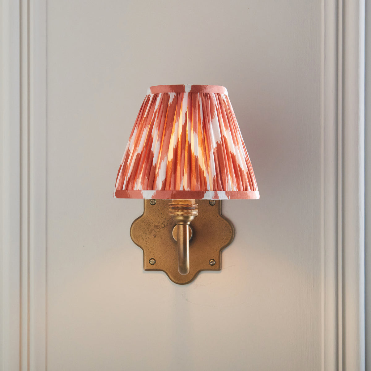 Front view of the Anvil Curve wall light with lit pink-orange zigzag ikat shade on quatrefoil plate