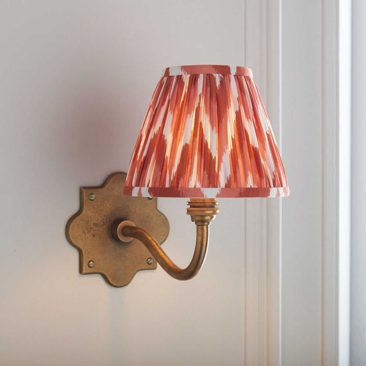 Anvil Curve antique brass wall light angled on panelling with vivid orange zigzag ikat shade