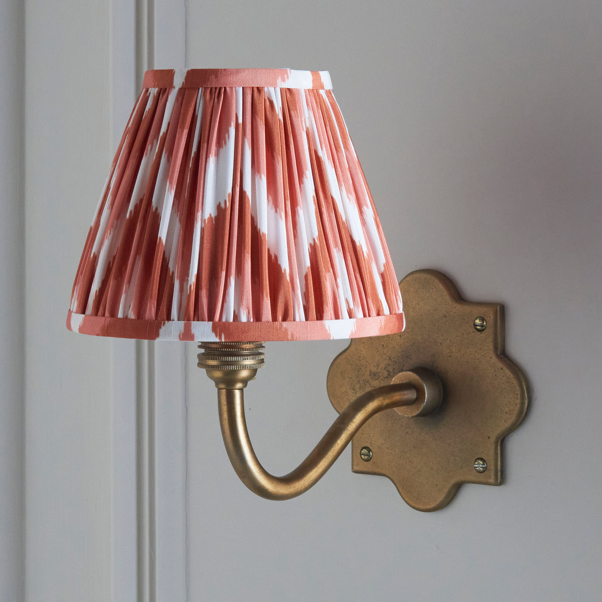 Lit Anvil Curve wall light on pale panelling, pink and white zigzag ikat pleated shade
