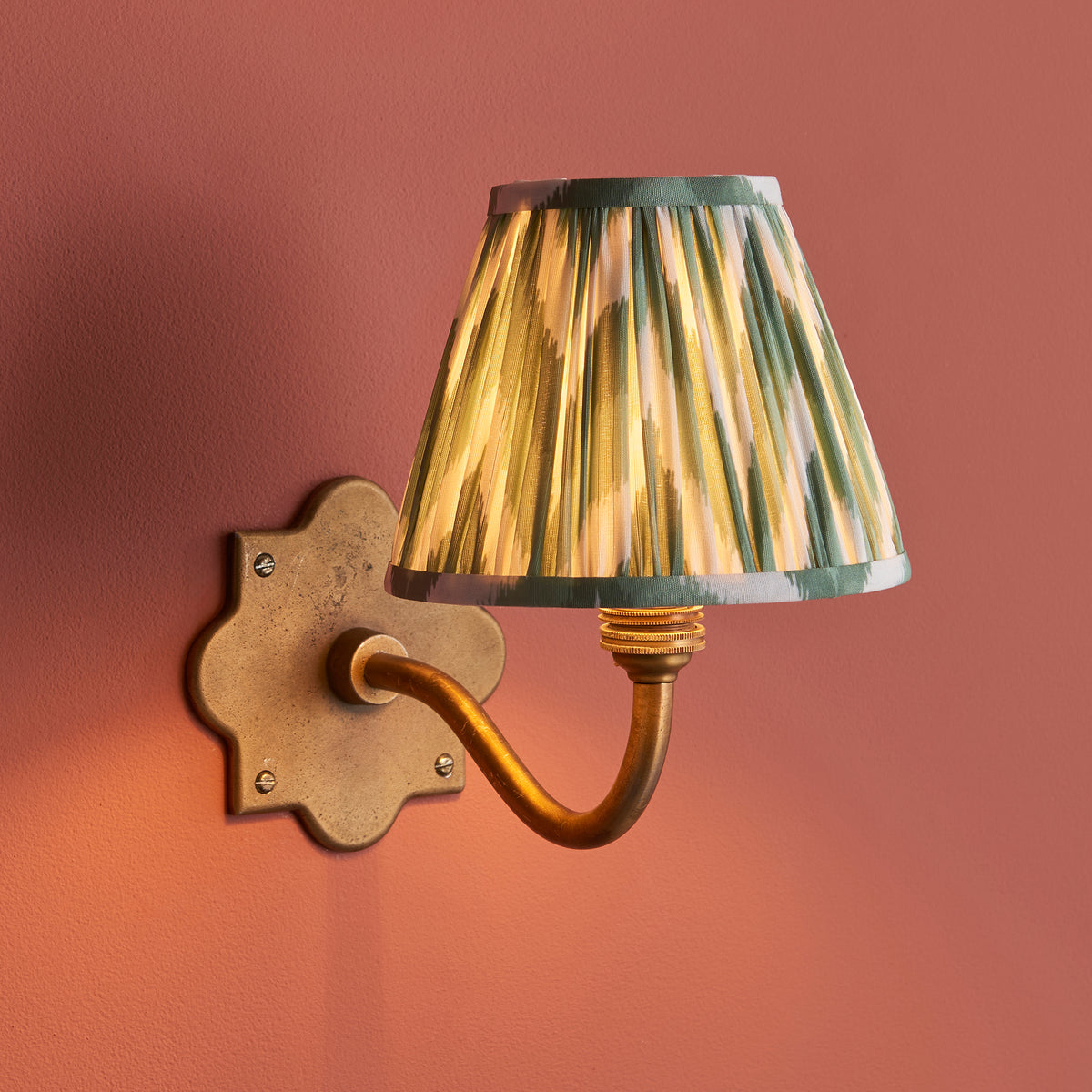 Anvil Curve wall light on a terracotta wall, green zigzag ikat pleated shade glowing warmly