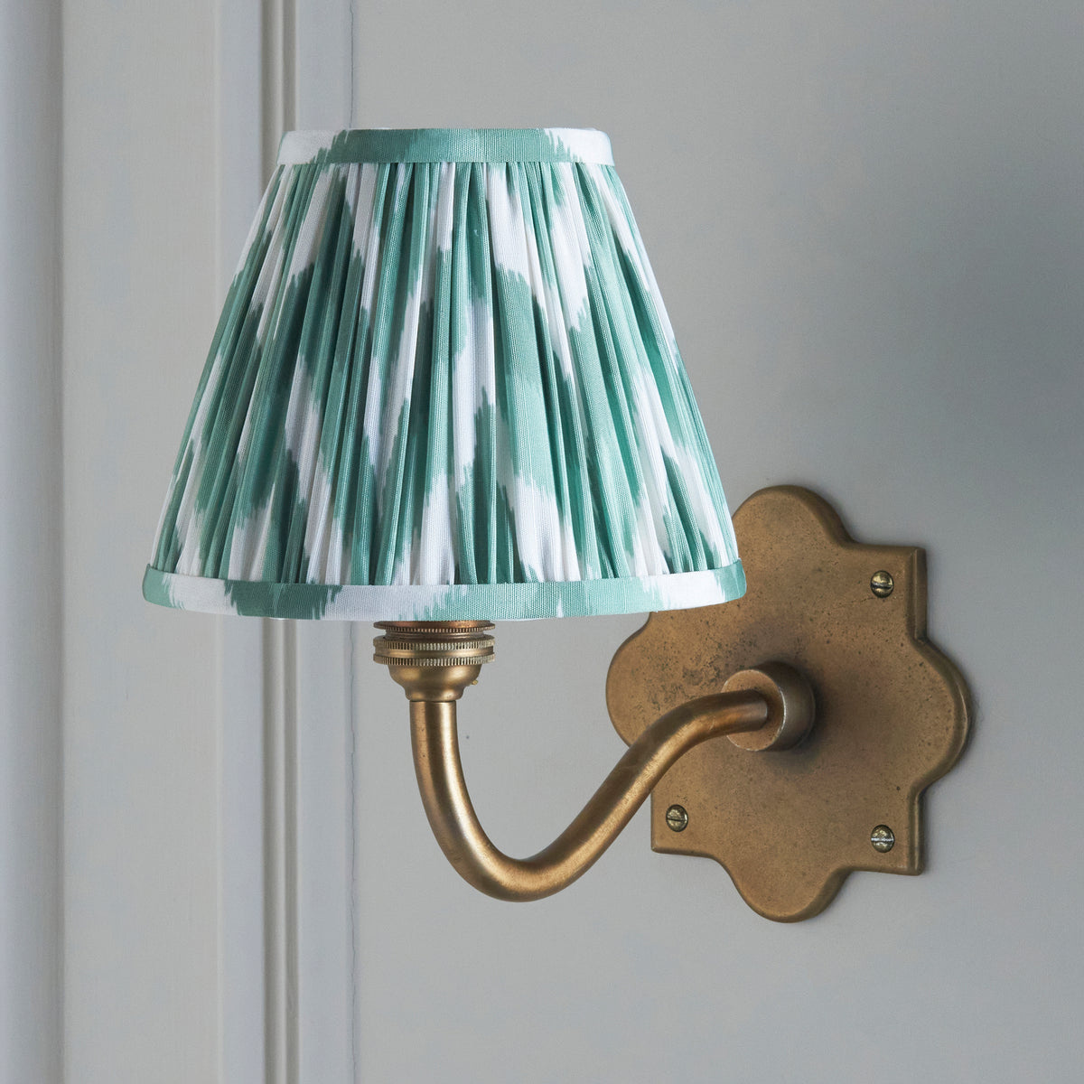 Lit Anvil Curve wall light on pale panelling, mint and cream zigzag ikat pleated shade