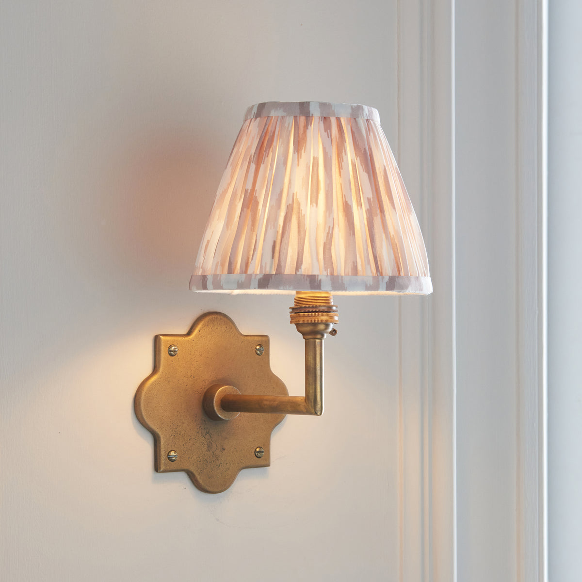 Anvil Angle antique brass wall light angled on panelling with taupe and cream ikat pleated shade
