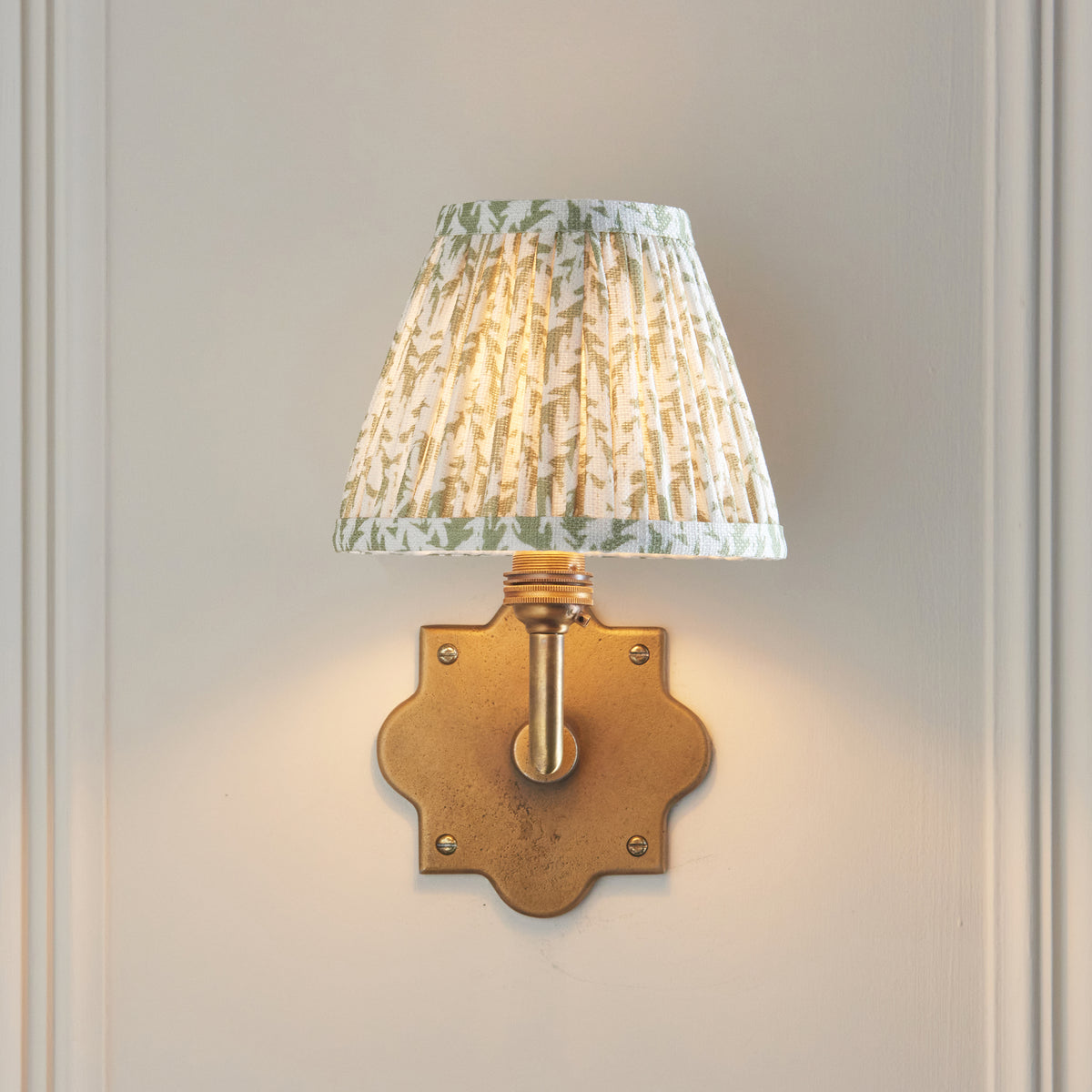 Front view of the Anvil Angle & Leaf wall light, lit leaf-print shade on a quatrefoil brass plate