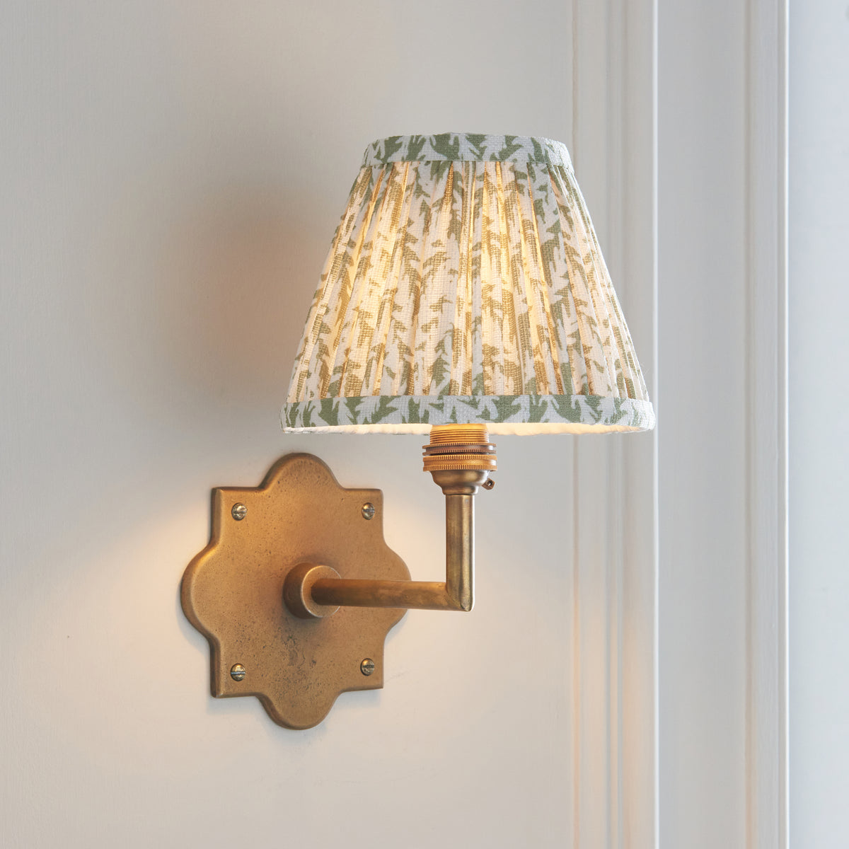 Anvil Angle & Leaf brass wall light angled on panelling with green leaf-patterned pleated shade