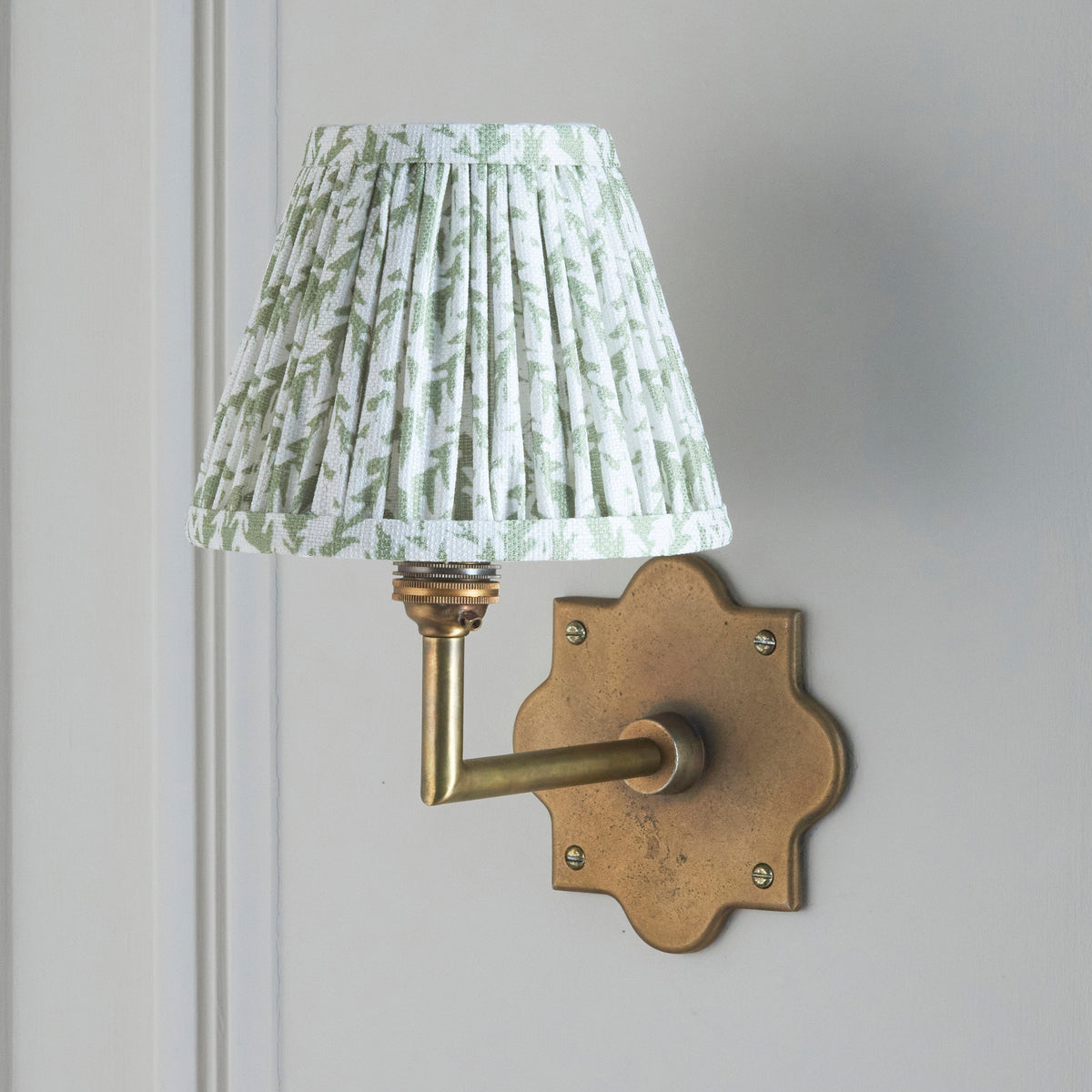 Anvil Angle & Leaf wall light on grey-white panelling, crisp green leaf-print pleated shade