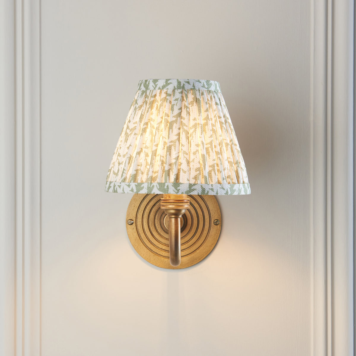 Ripple Curve & Leaf brass wall light seen head-on, ribbed circular backplate and lit leaf-print shade