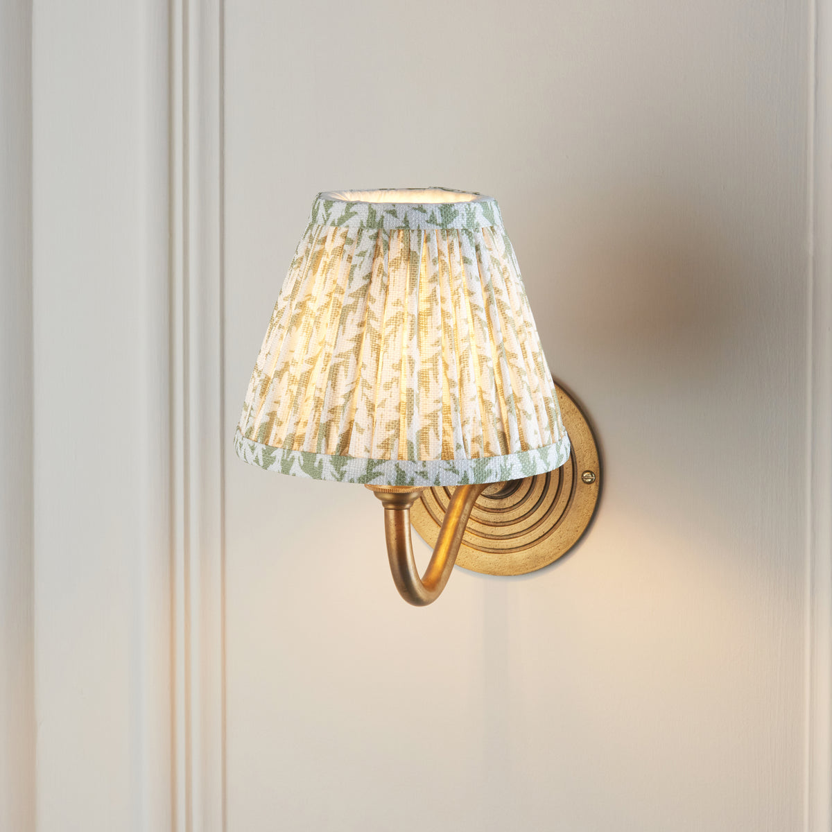 Ripple Curve & Leaf brass wall light on a grey wall, swan-neck arm and pleated leaf-print shade