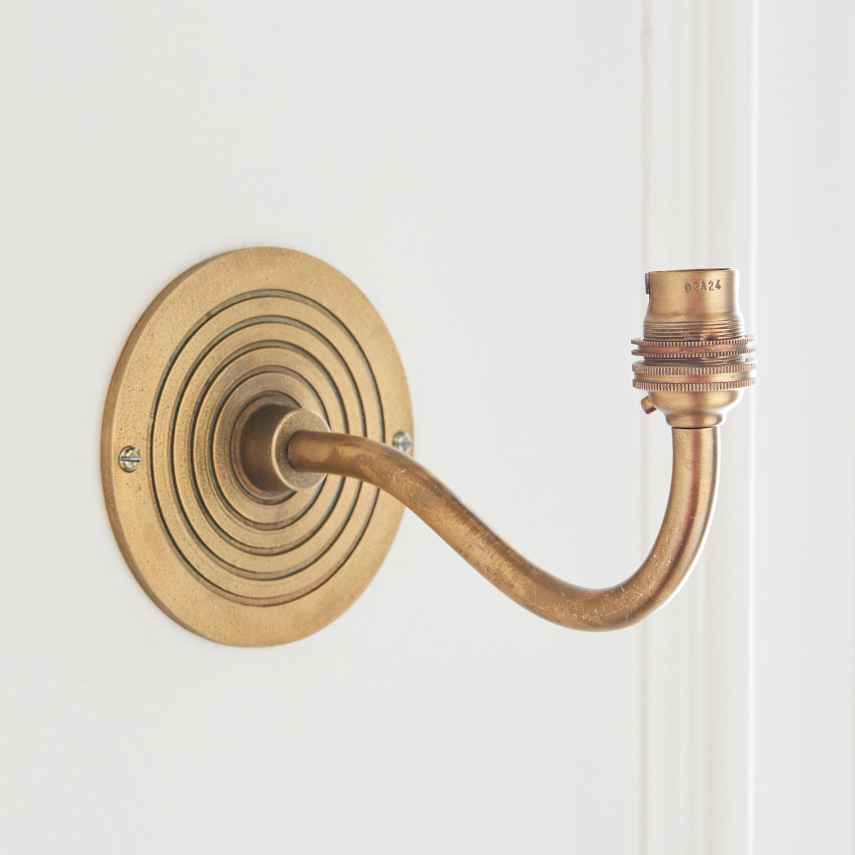 Antique brass swan-neck wall bracket with ribbed round backplate, shown without a shade