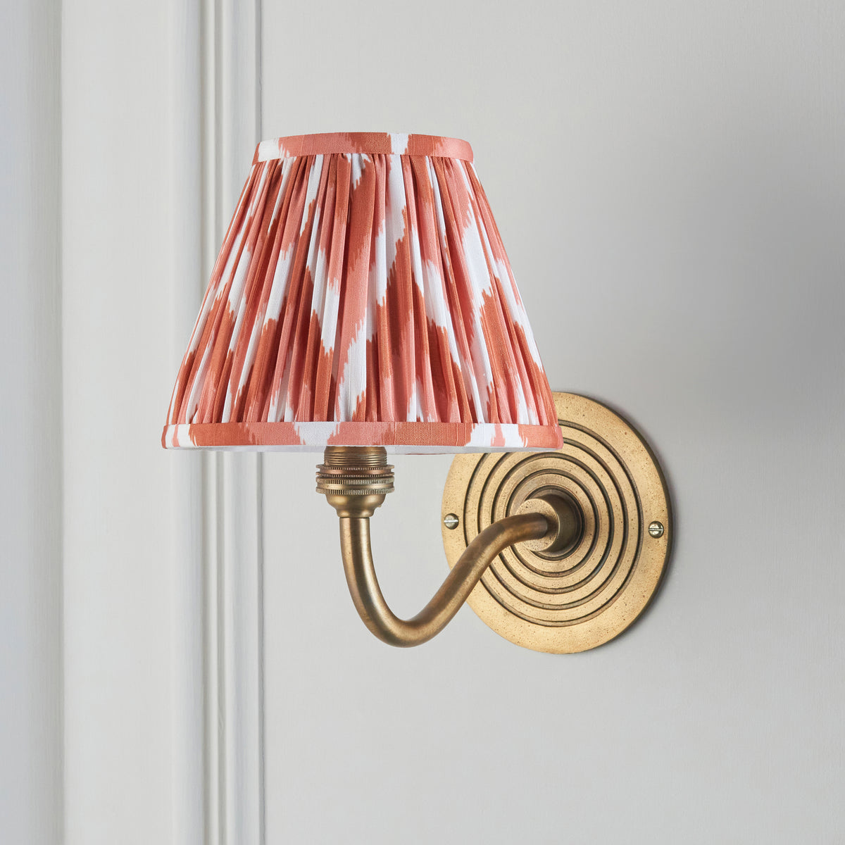 Ripple Curve brass wall light on grey panelling, soft pink ikat pleated shade and swan-neck arm