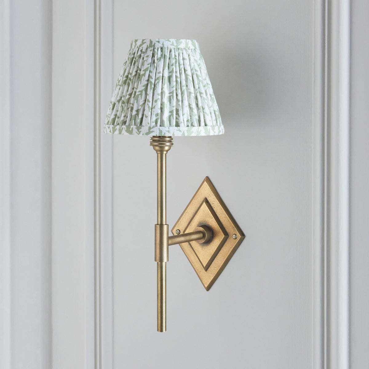 Diamond Tall brass wall light on a grey wall, tall stem and pleated green leaf shade illuminated