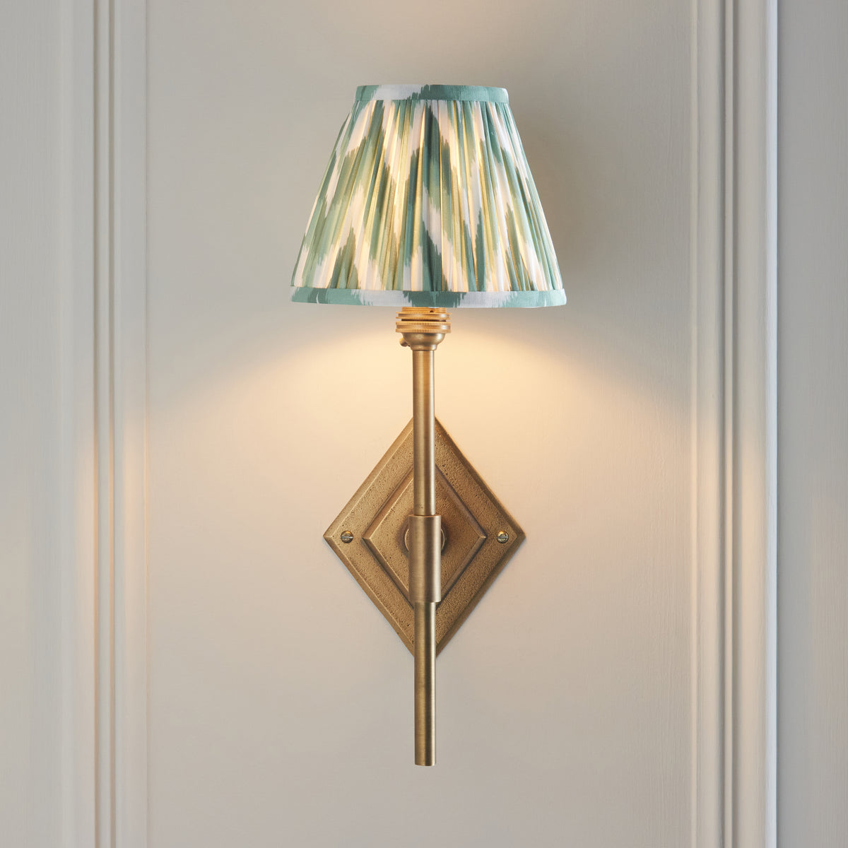 Diamond Tall brass wall light head-on against pale panelling, glowing green ikat shade on a slim stem