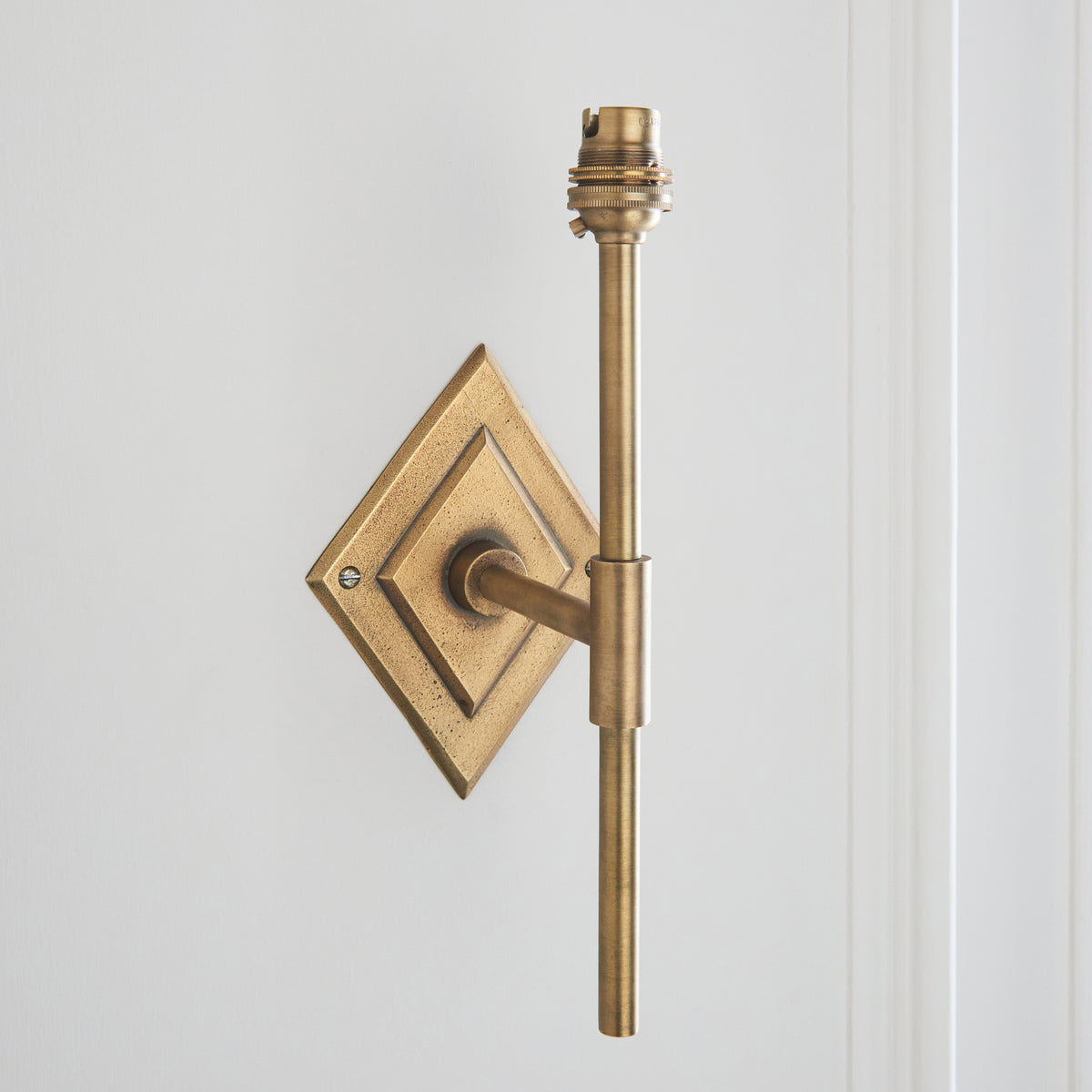 Tall brass wall bracket with diamond backplate and exposed lampholder, photographed shadeless