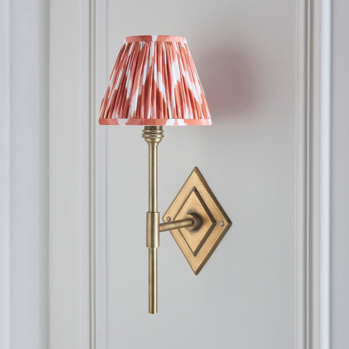 Diamond Tall brass wall light on grey panelling, soft pink ikat pleated shade and tall brass stem