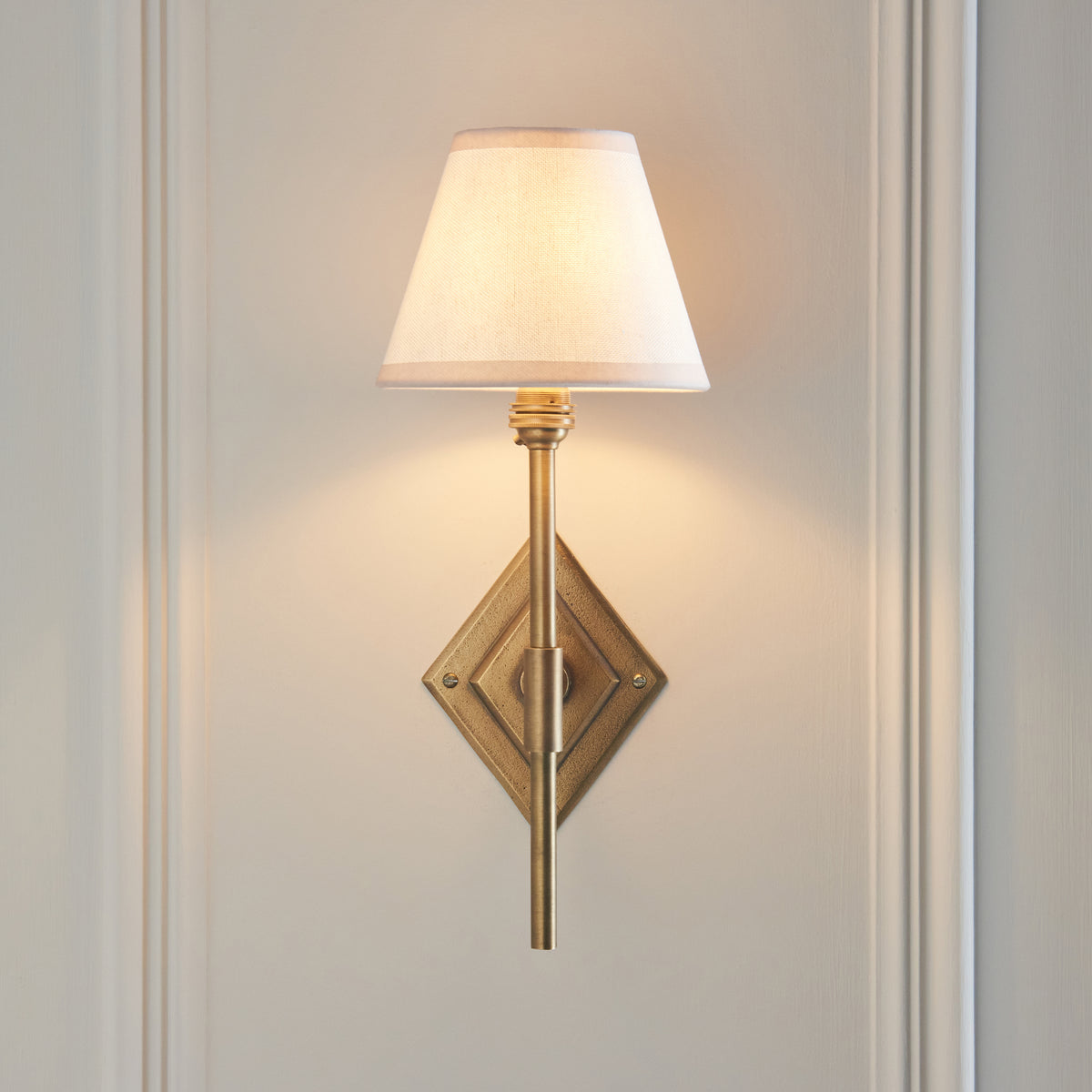 Diamond Tall brass wall light head-on against pale panelling, white fabric shade on a slim stem