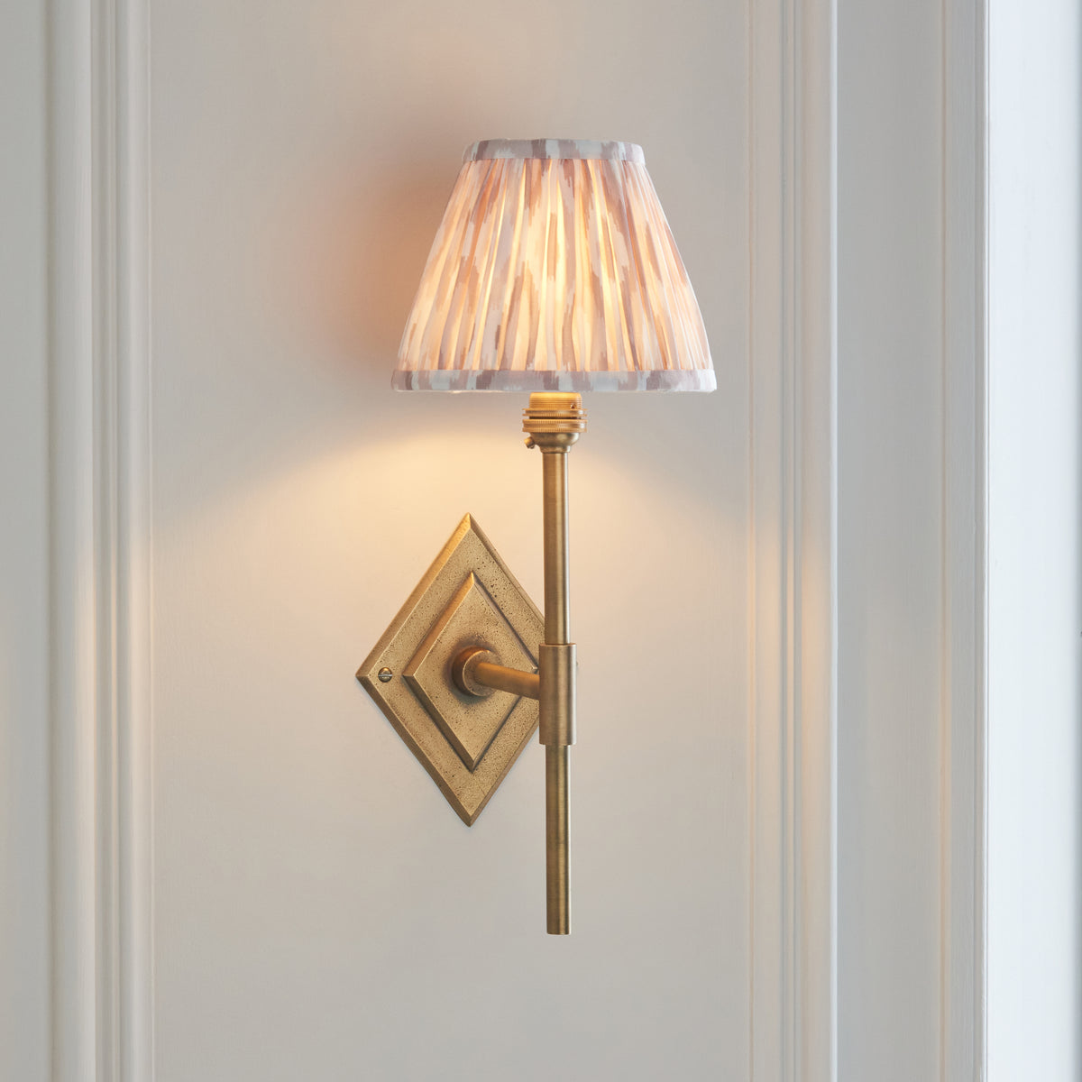 Angled view of the Diamond brass wall light showing diamond backplate and natural ikat pleated shade