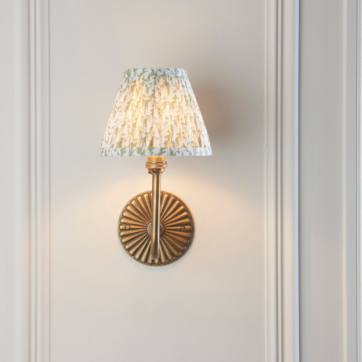 Front view of the Dahlia Swan wall light, ribbed brass backplate and green leaf pleated shade